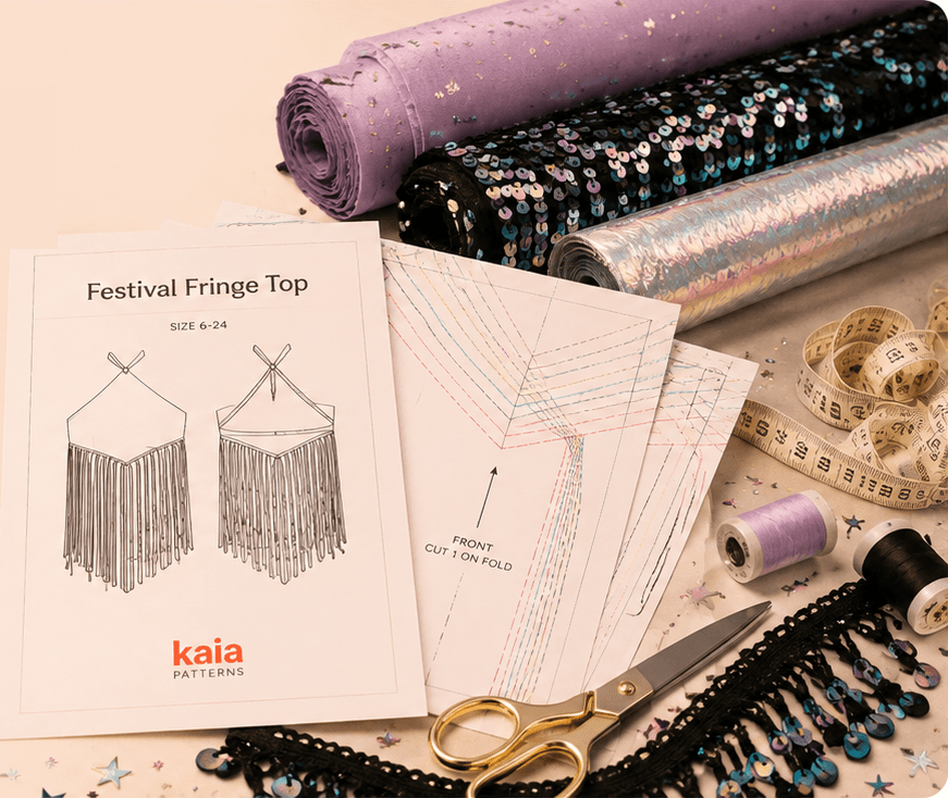 A Kaia Patterns Festival Fringe Top pattern envelope beside printed pattern tissue, rolls of sequinned and iridescent fabric, gold scissors, thread and a tape measure.
